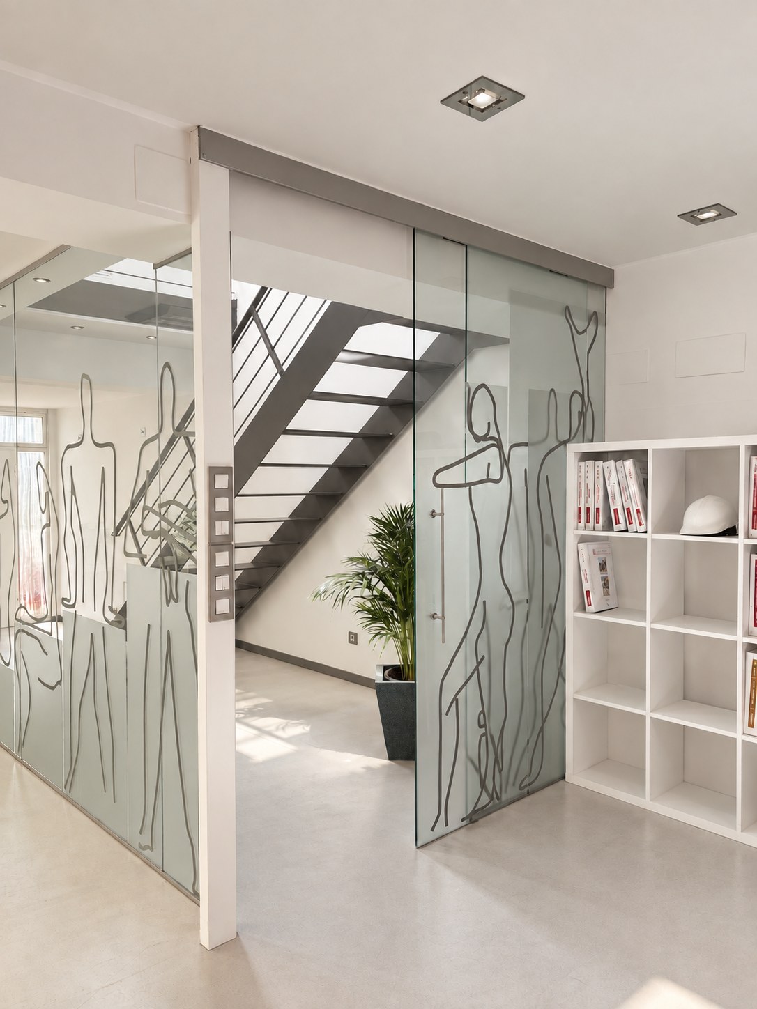 Estudio ERD Arquitectos: puerta corredera de vidrio con figuras dibujadas, escalera metálica y estantería blanca